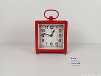 Front view of red metal alarm clock showing dial and overall appearance