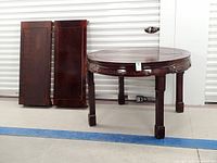 Round rosewood dining table with two separate leaves leaning on wall