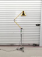 Full view of articulated yellow floor lamp on chrome pole and caster base