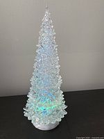 Full view of illuminated transparent Christmas tree on white base