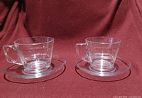 Two clear glass cups each on a saucer, frontal view