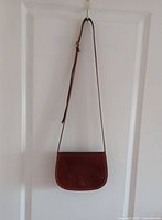 Full view of leather crossbody bag hanging, showing size, color and overall condition