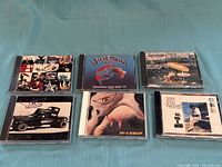 Six rock music CDs: U2 Achtung Baby, Steve Miller Band Greatest Hits 1974-78, Supertramp Crisis? What Crisis?, Aerosmith Pump, Aerosmith Get a Grip, Stevie Ray Vaughan Greatest Hits in jewel cases