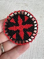 Front view of circular red and black beaded pendant held in hand