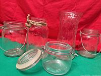 Five clear glass items arranged together: four Bernardin jars and one fluted vase
