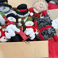 Open box showing assortment of plush snowmen, Santa figure, Mrs. Claus and wooden sled