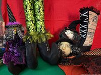 Group of stuffed witch decorations showing doll, large legs with boots, boot with witch face