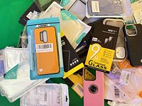 Pile of packaged phone cases and NEW'C tempered glass protectors showing variety
