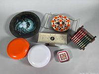 Group shot of all items: weather station, enamel bowl, trivet, ashtrays, tin box, book set