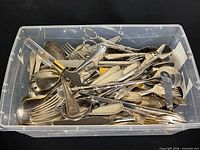 Plastic tub filled with assorted silver-tone cutlery and utensils