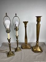 Two brass table lamps and two brass pillar candleholders side by side