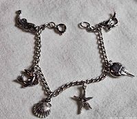 Full view of silver-tone charm bracelet with five ocean charms displayed on fabric background