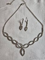 Full view of necklace and both earrings on cloth background