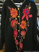 Full view of black floral Storybook Knits sweater hanging