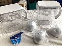 Two pitchers, white lids, four sealed filter cartridges on table