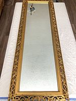 Full-length rectangular wall mirror with gold-tone openwork frame lying flat on table