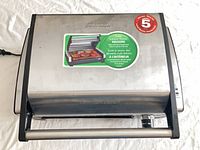 Closed Hamilton Beach stainless steel countertop grill showing exterior and sticker