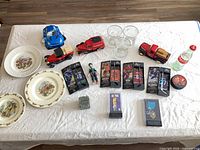 All items laid out: plates, diecast vehicles, boxed figures, glasses, bottle, puck, coin, puzzle cube, anime figure