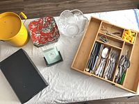 Full lot overview showing yellow pail, red plates, clear bowl, black box, napkin holder, and utensil tray with flatware