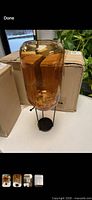 Full view of amber crackle glass vase on black metal stand with packaging boxes behind