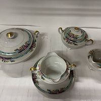 Four porcelain serving pieces including covered serving bowl, sugar bowl, gravy boat on underplate, and creamer, all in matching pattern