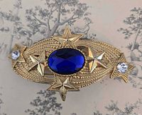 Front view of large oval brooch showing blue cabochon, star accents, rhinestones, beaded border