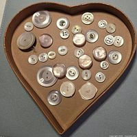White, ivory and pink shell or mother of pearl buttons displayed in heart tray