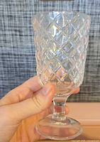 Hand holding one unwrapped pressed glass goblet showing diamond pattern and stem