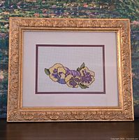 Front view of framed pansy cross stitch showing full artwork and ornate gold frame