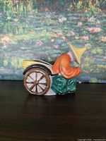 Left side view of glazed ceramic rickshaw planter showing seated figure, wheel and cavity opening