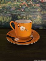 Teacup on saucer showing orange glaze, blossom motif, gilt rim