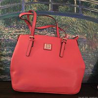 Front view of coral pebbled-leather tote showing logo plate and straps