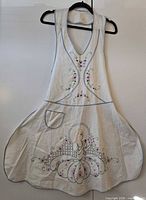 Front view of off-white embroidered full-bib apron on hanger