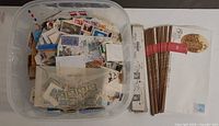 Top view of plastic tub filled with loose stamps, illustrated covers alongside, and boxes of Hawid mounts