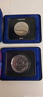 Both coins in their individual cases, 1972 above 1975 below