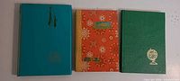 Three closed albums: teal, orange with snowflakes, green with gold globe