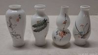 Front view of four porcelain bud vases showing painted motifs and shapes
