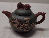 Side view of teapot showing dragon relief, spout, handle, lid finial
