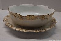 Serving bowl nested on underplate showing gilt scalloped edges and color.