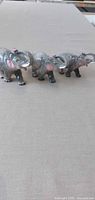 Three gray glazed ceramic elephant figurines lined up on fabric surface