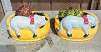 Pair of yellow ceramic planters with blue cat motifs, succulents visible