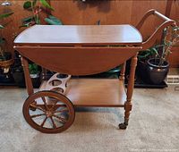 side view showing drop leaf folded, large spoked wheel, lower shelf with bottle cutouts