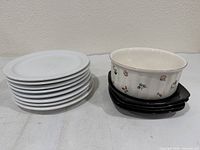 Stack of eight white round plates beside five black square plates with Villeroy & Boch Petite Fleur bowl on top