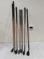 Full view of seven wooden-shaft golf clubs standing against wall