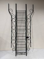 Full view of tall black metal rack with wire shelves and scrollwork sides