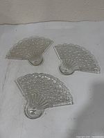 Three identical clear pressed glass fan-shaped dishes displayed