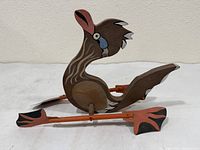 Left side view of carved wooden bird whirligig showing body shape, paddle blades attached to axle