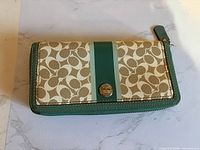 Front view of Coach zip-around wallet showing signature canvas, teal stripe and metal medallion