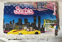Folded blanket showing Barbie logo, skyline, yellow convertible, fringe