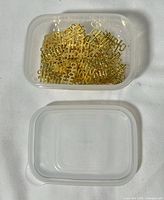 Plastic container filled with gold-tone Double Happiness metal pieces next to lid